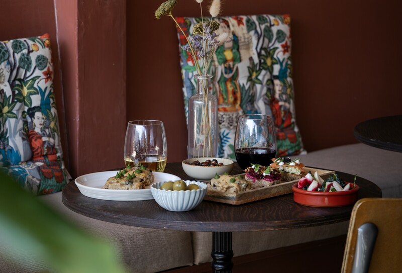 Counter Culture, Newquay, Cornwall — relaxed dining table with small plates, glasses of wine, and vibrant Mediterranean-style cushions — South West regional winner, Best Local Restaurant 2025 in The Good Food Guide.